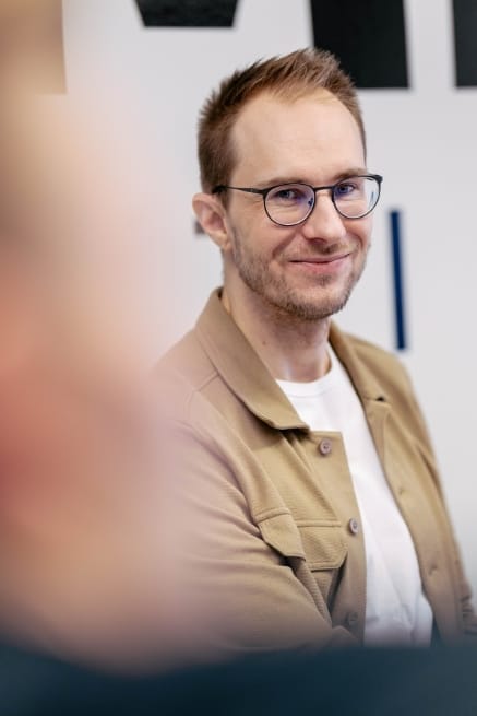 Kuvassa henkilöllä on päällään valkoinen ja beige paita, henkilöllä on silmälasit ja hän hymyilee kameraan.